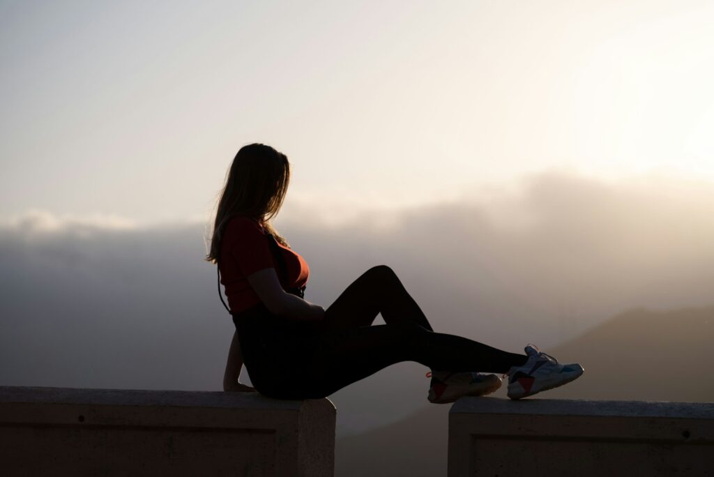 woman in red tank top and black pants sitting on concrete bench during daytime